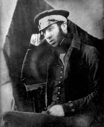 A daguerreotype portrait of a young bearded man in a Royal Navy undress coat and cap, seated, one hand raised to his temple.